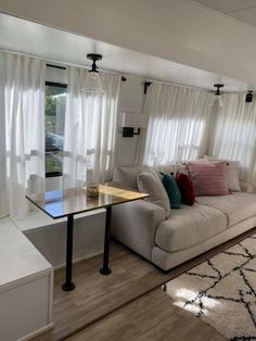 a living room filled with furniture next to a window covered in white drapes and curtains