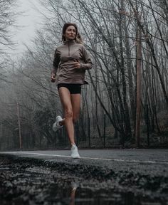 a woman is running in the rain with trees behind her and water on the ground