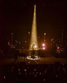 a person sitting at a table in front of a microphone on stage with lights behind them