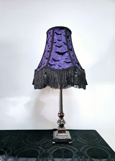 a lamp that is sitting on top of a table with a purple shade over it