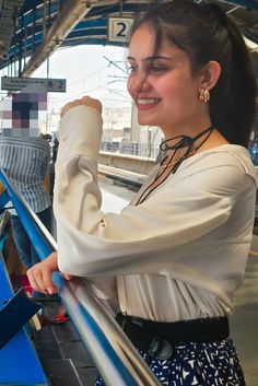 a woman standing on top of a blue and white train platform holding onto a rail