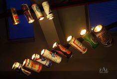 several beer cans hanging from the ceiling with lit candles in front of them and one light on top