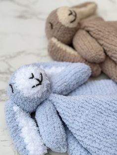 two knitted teddy bears laying next to each other on a marble counter top, one with its eyes closed