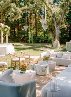 an outdoor seating area with white couches, tables and chandeliers hanging from the trees