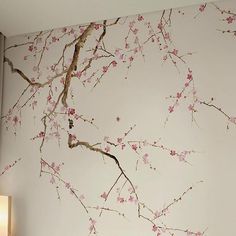 the wall is painted with pink flowers and branches on it, along with a lamp