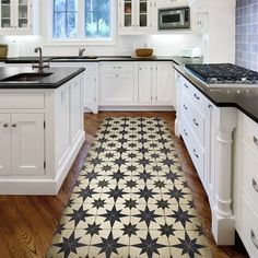 a kitchen with white cabinets and black counter tops on a wooden floor, along with an area rug that looks like a star pattern