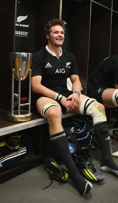 two rugby players are sitting in the locker room with their legs wrapped around each other