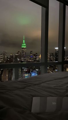 a laptop computer sitting on top of a bed in front of a window overlooking a city