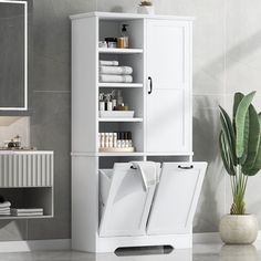 a white cabinet with towels and other items on it next to a plant in a bathroom