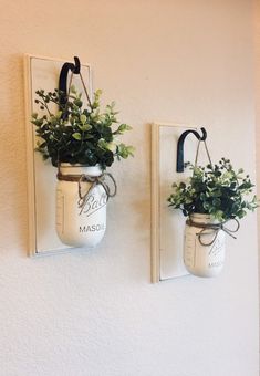 two mason jars with plants hanging on the wall