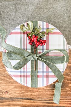 a plaid plate with holly and berries tied around it on a wooden tablecloth covered placemat