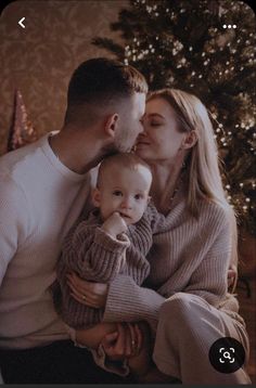 a man and woman holding a baby in front of a christmas tree