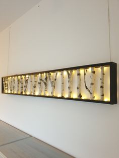 a wall mounted light up sign with lights on it's sides and birch trees in the background