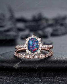 an opal and diamond ring set on top of a black stone slab with other jewelry items in the background