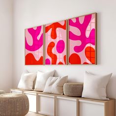 two pink and red paintings hanging on the wall next to a white bench with pillows