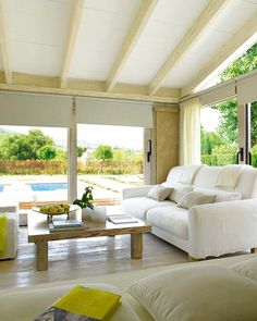 a living room filled with white furniture next to a large glass wall window overlooking a pool