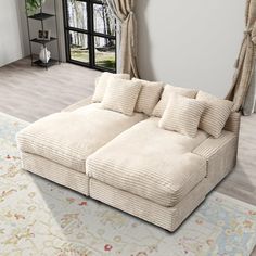 a large white couch sitting in front of a window next to a rug on top of a hard wood floor