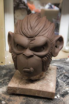 a clay sculpture of a demon head on a piece of wooden workbench with other items in the background