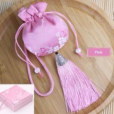 a small pink purse with tassels on top of a wooden tray next to a box