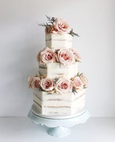 a three tiered cake with pink flowers on top is sitting on a white pedestal