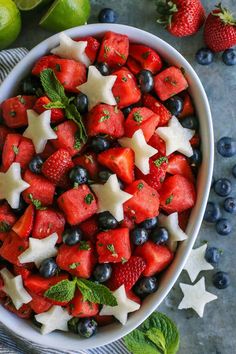 a bowl filled with watermelon, blueberries and star shaped strawberries next to limes