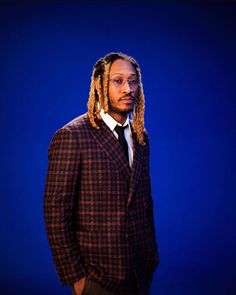 a man with dreadlocks standing in front of a blue background wearing a suit and tie