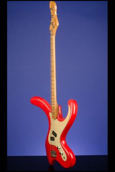 a red electric guitar sitting on top of a black table next to a blue background