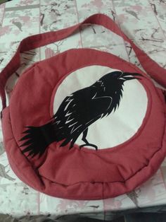 a red bag with a black bird on it sitting on a tablecloth covered surface