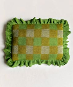 a green and beige pillow with ruffles on the bottom, sitting on a white surface