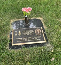 a small vase with pink flowers in it sitting on a black plaque surrounded by green grass