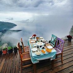 the table is set for two on the wooden deck overlooking the water and mountains in the distance