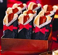 hotdogs wrapped in paper with red bows are sitting in a box on a table