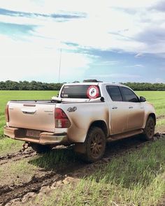 a truck parked in the middle of a dirt road near a field with green grass