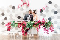 a bride and groom sitting at a table with pink flowers in front of the wall