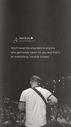 a man standing in front of a crowd holding a guitar and looking at the sky