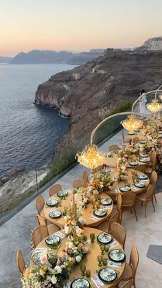 an outdoor dining area overlooking the ocean at sunset with flowers and plates laid out on it