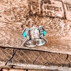 a silver ring with turquoise stones sitting on top of a piece of wood