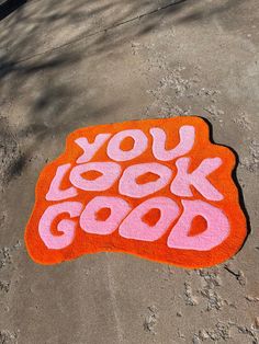 an orange and pink rug with the words you look good painted on it in front of a tree