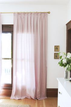 a pink curtain hangs in front of a window with wooden floors and white walls, along with a rug on the floor