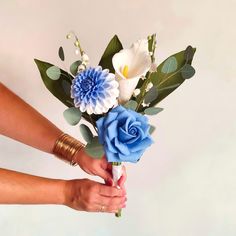 a woman holding a bouquet of flowers in her hand with blue and white flowers on it