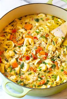 a pot filled with pasta and vegetables on top of a white countertop next to a wooden spoon