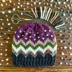 a knitted hat sitting on top of a wooden table next to scissors and thread