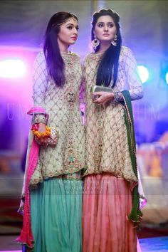 two women in long dresses standing next to each other on a stage with lights behind them