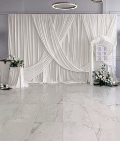 a white wedding ceremony setup with drapes and flowers in vases on the floor