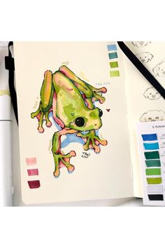 a drawing of a frog on paper next to color swatches and marker pens with markers