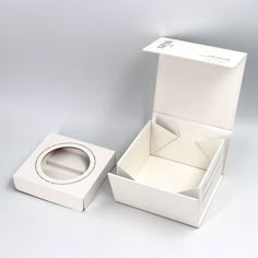 an open box with a ring inside on a white surface, next to it's lid