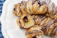 chocolate covered croissants on a plate with powdered sugar and drizzled