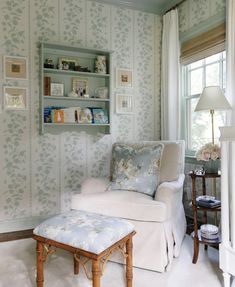 a white chair and ottoman in a room with wallpapered walls, windows, and a lamp