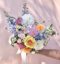 a bouquet of flowers is being held by someone's hand in front of a pink wall