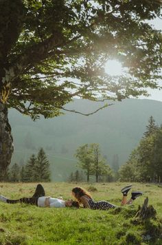 two people laying in the grass under a tree